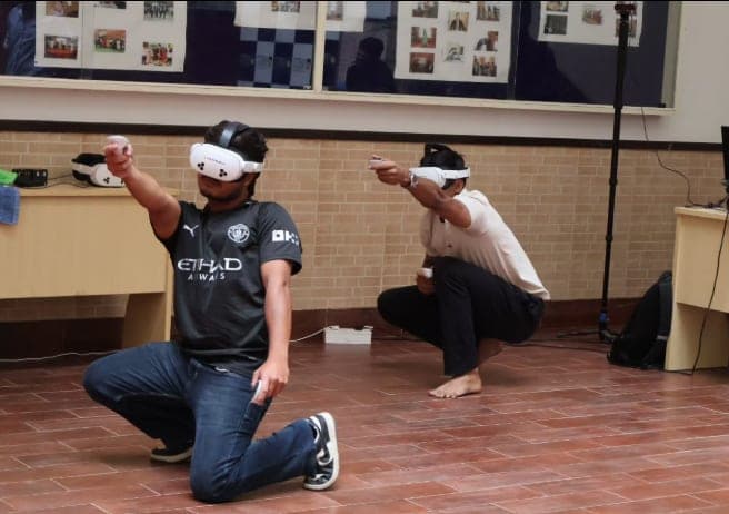 Two students exploring a shared virtual scene in VR headsets, one kneeling in the foreground to take aim