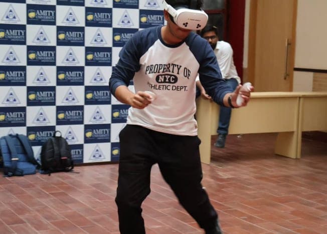 A student on their feet, moving through a virtual environment with a VR headset and hand controllers